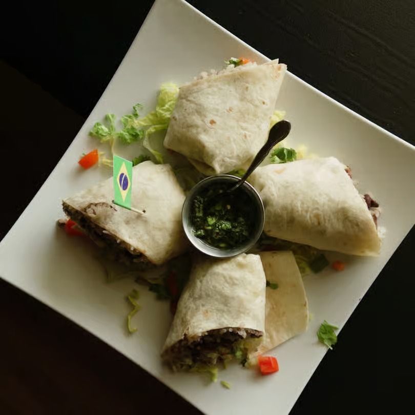 Four tortilla wraps arranged like petals around a small bowl of green dipping sauce on a white plate.