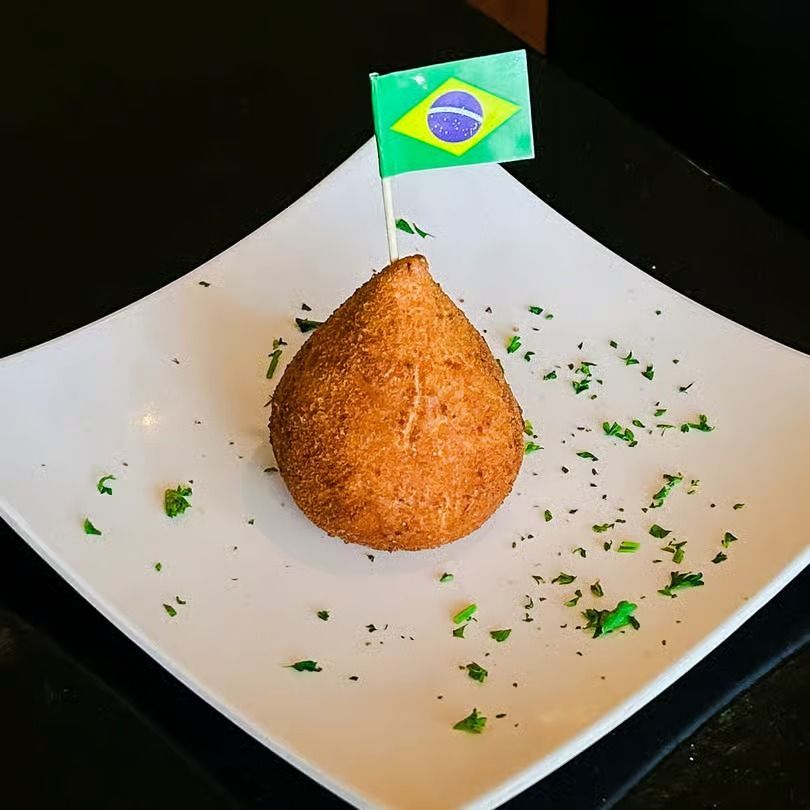 Brazilian flag toothpick in a breaded teardrop snack on a white plate with herbs