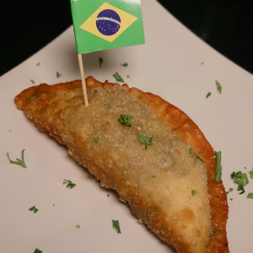 Brazilian fried pastry with a small Brazil flag garnish on a white plate, sprinkled with herbs