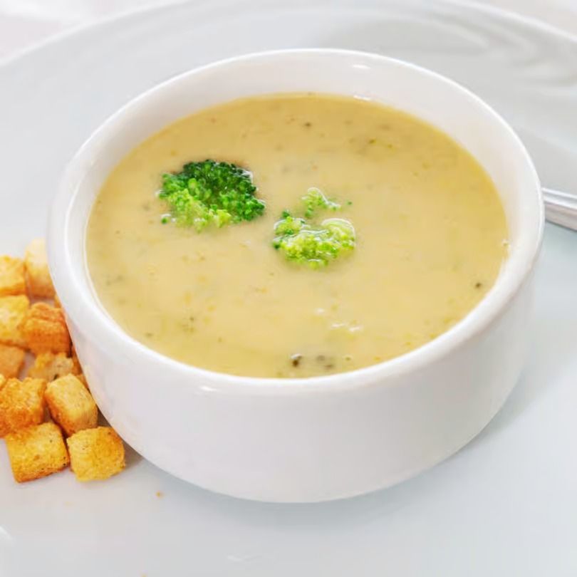 Bowl of creamy broccoli soup with croutons on a white plate