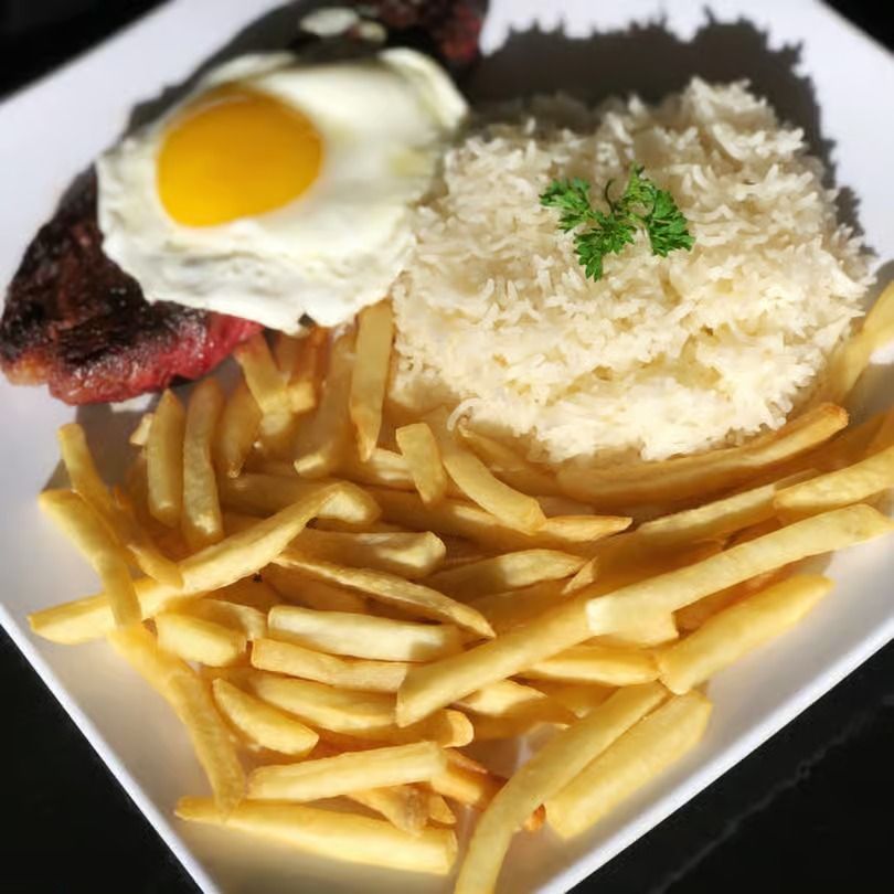 Plate of fries with a sunny-side-up egg, shredded cheese, and grilled meat on a white plate