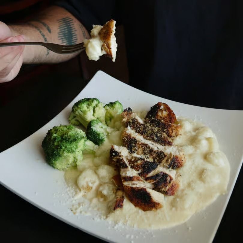 Grilled chicken with creamy mashed potatoes and broccoli on a white plate, with a fork holding a bite above it