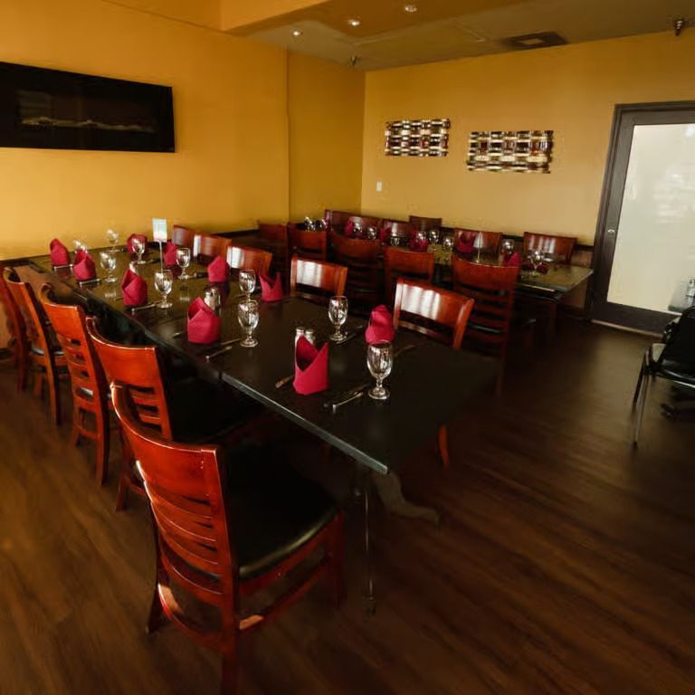 Empty restaurant dining room with set tables, red napkins, and wooden chairs on a dark floor.