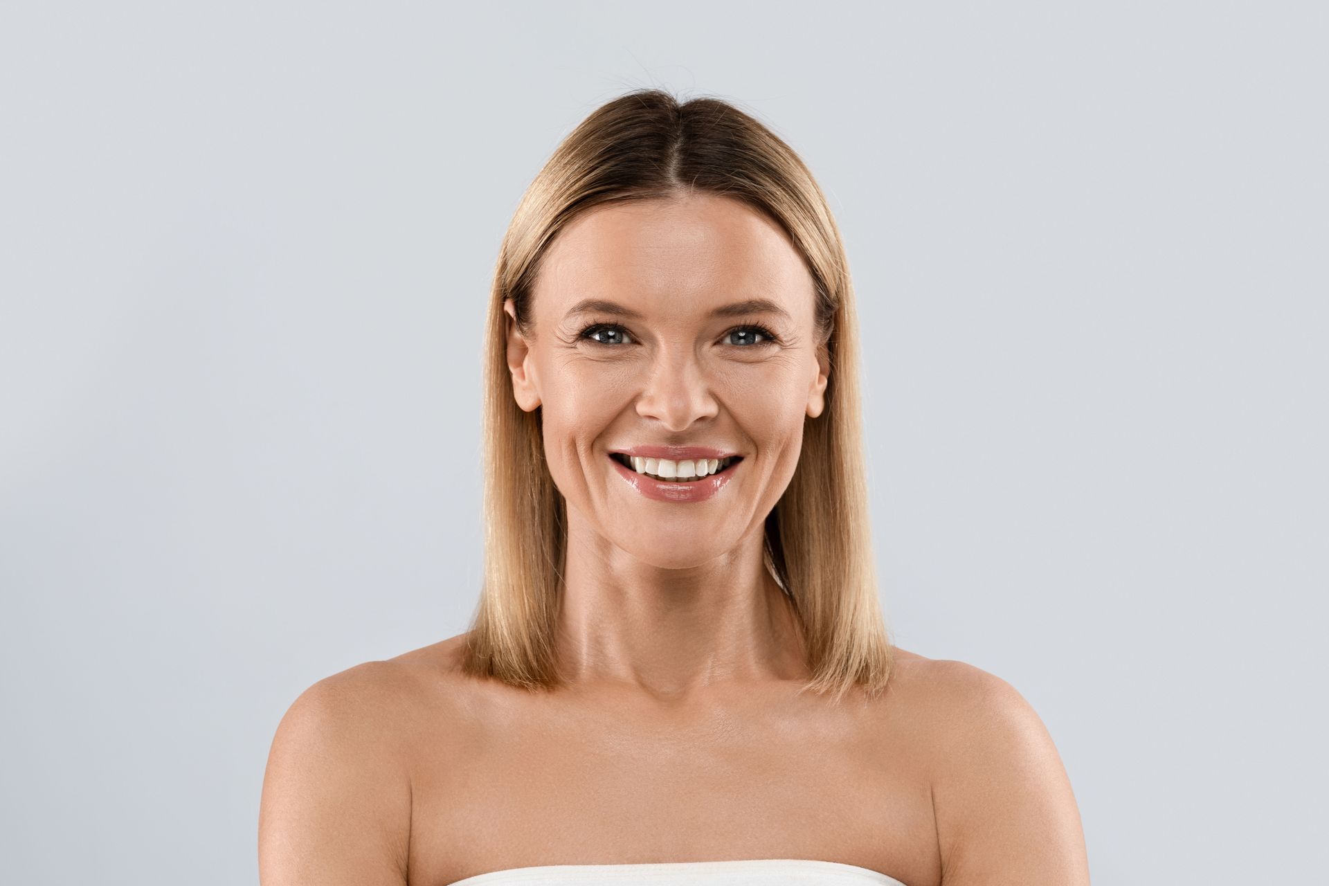 A woman wrapped in a white towel is smiling and looking at the camera.