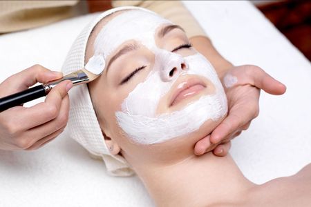 A woman is getting a white mask on her face.