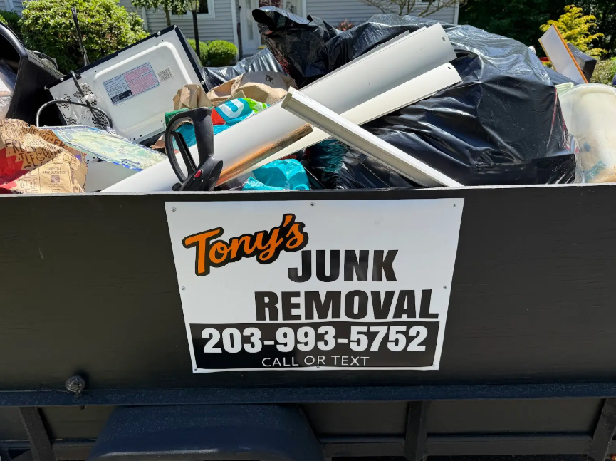 Tony's Junk Removal truck with a bin full of debris and a sign showing the company name and phone number.