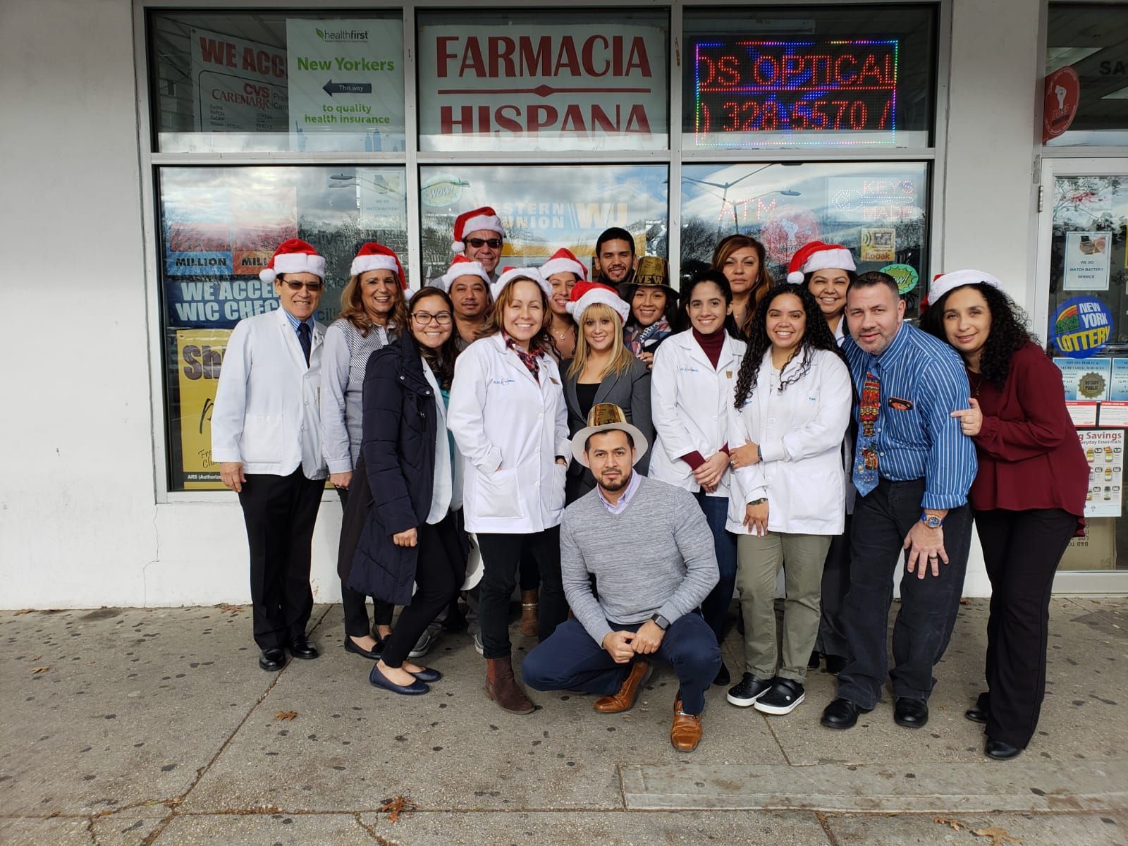 A group of people wearing santa hats are posing for a picture in front of a pharmacy.