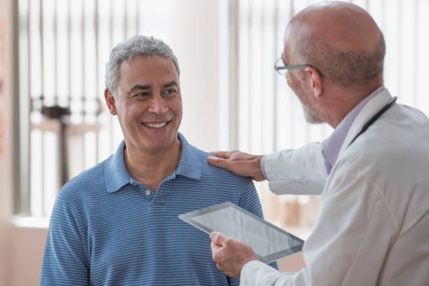 A doctor puts his hand on a man's shoulder while holding a tablet.