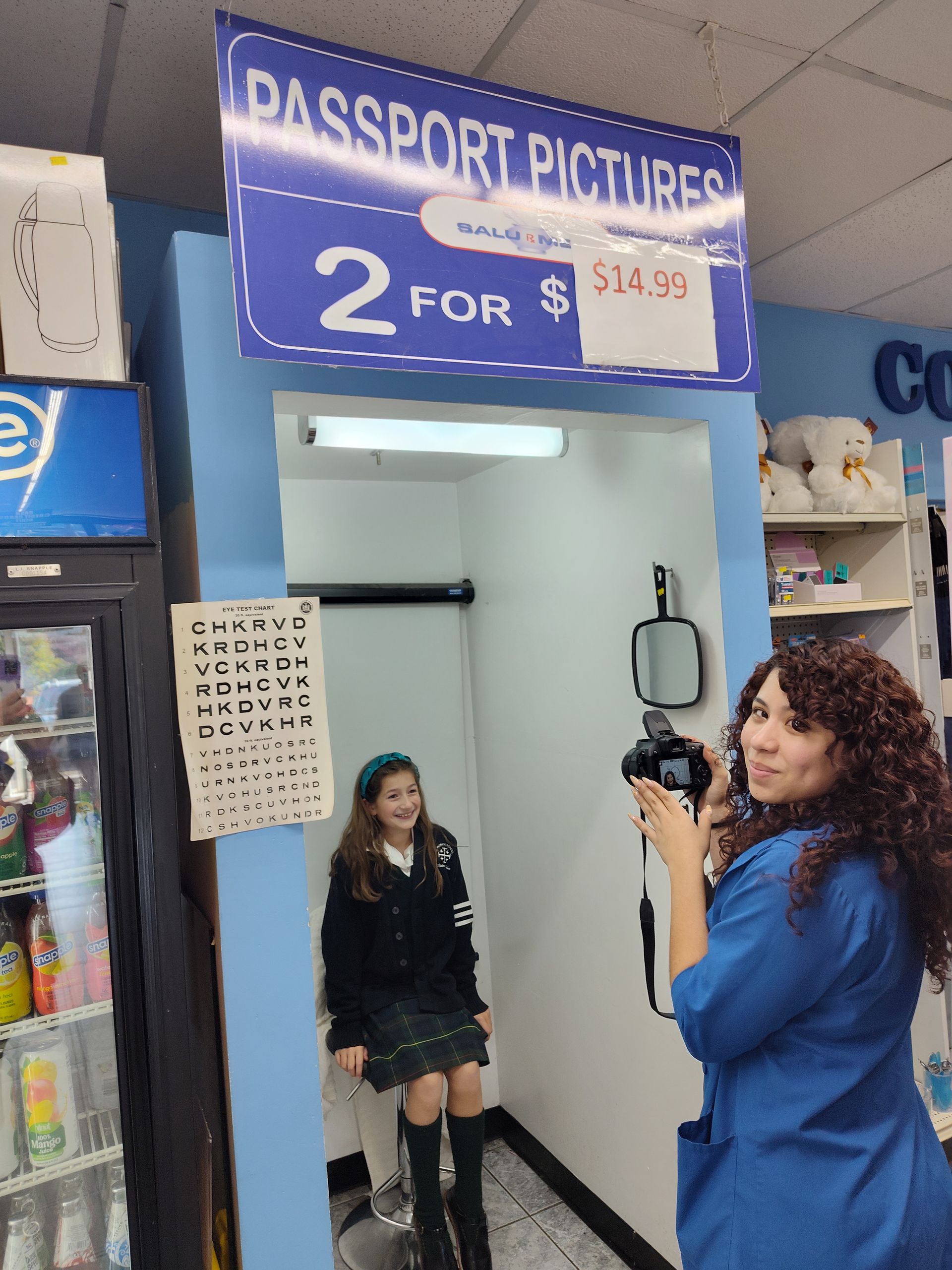 A woman is taking a picture of a girl under a sign that says passport pictures