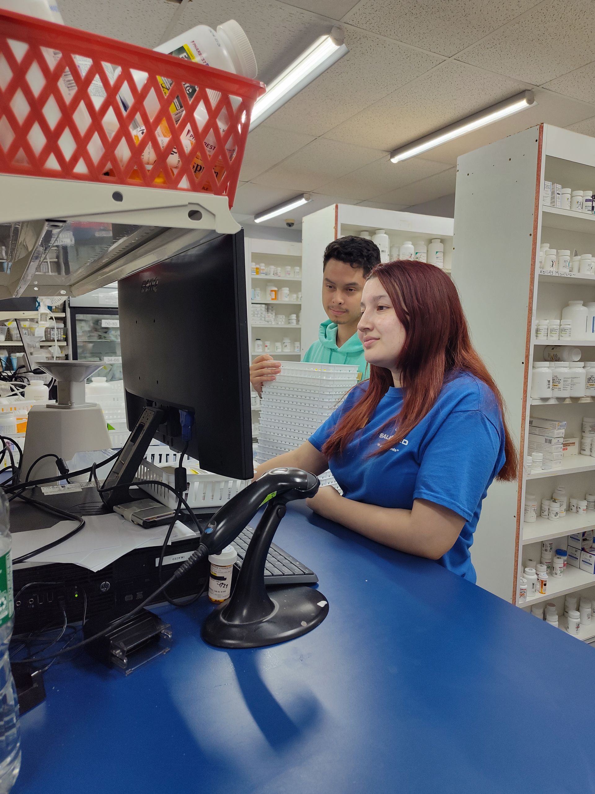 A woman is sitting at a counter in a pharmacy looking at a computer screen.