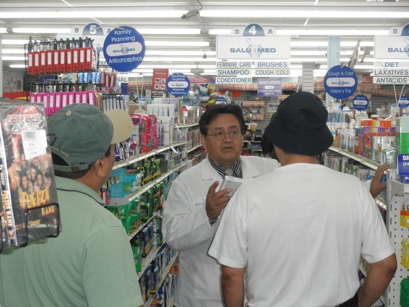 A man in a lab coat is talking to two other men in a pharmacy