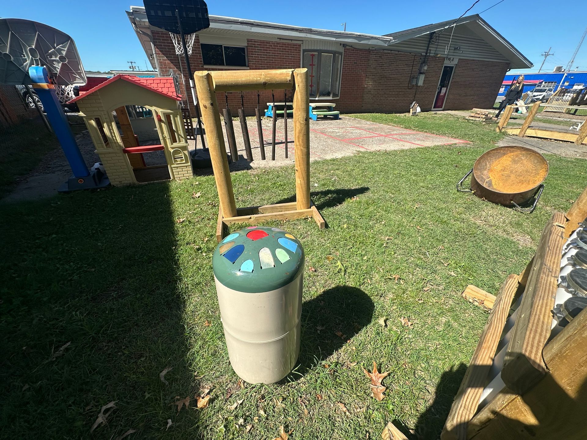 A trash can is sitting in the grass in front of a house.