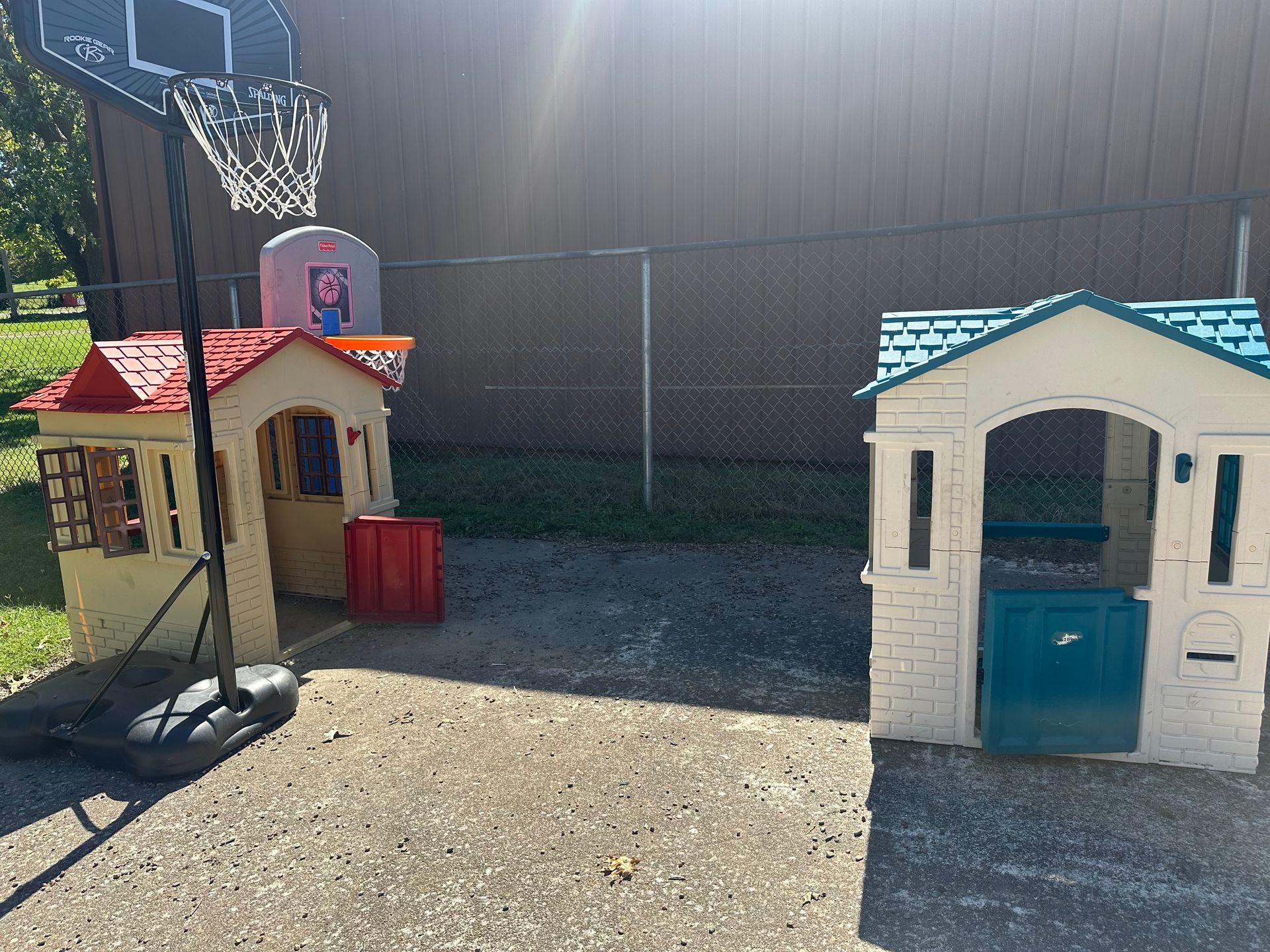 There are two playhouses and a basketball hoop in the backyard.