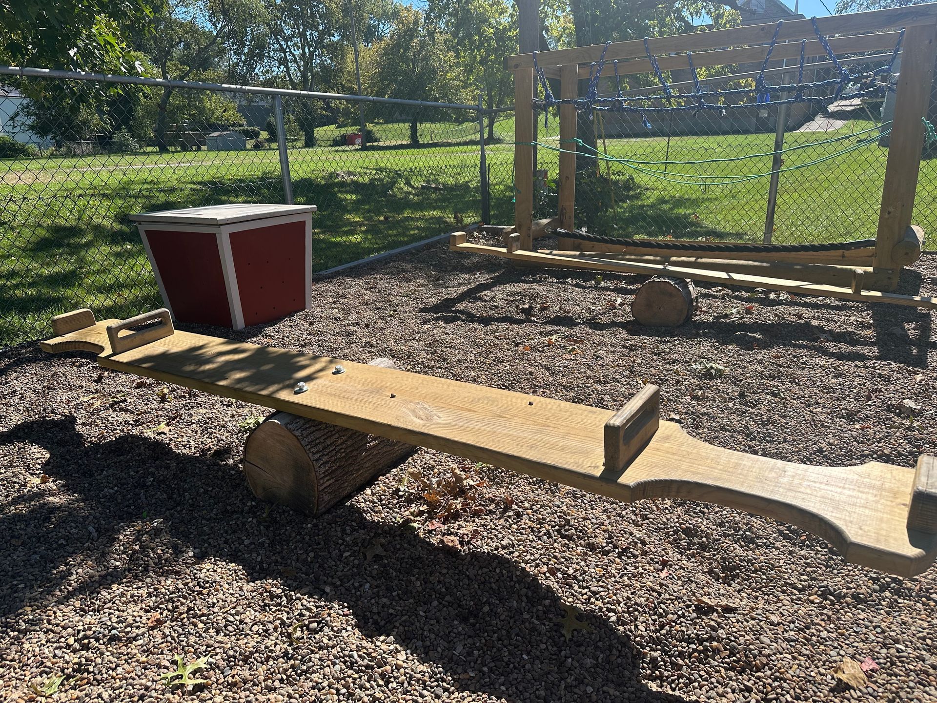 A wooden seesaw is sitting on top of a pile of gravel in a park.