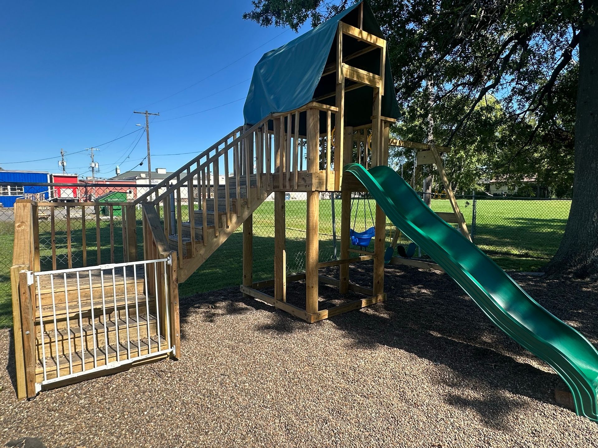 A wooden playground with a green slide and stairs.