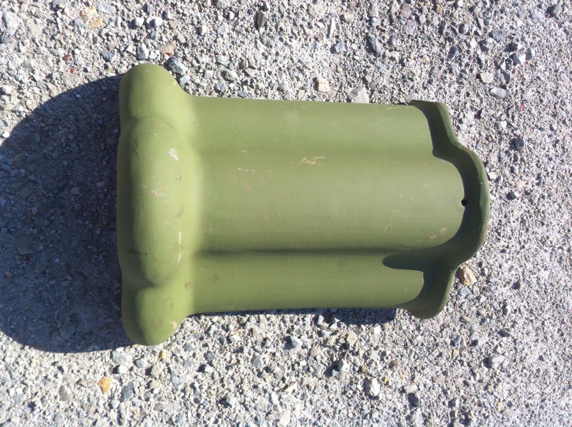 A green custom roof tile is sitting on a gravel surface