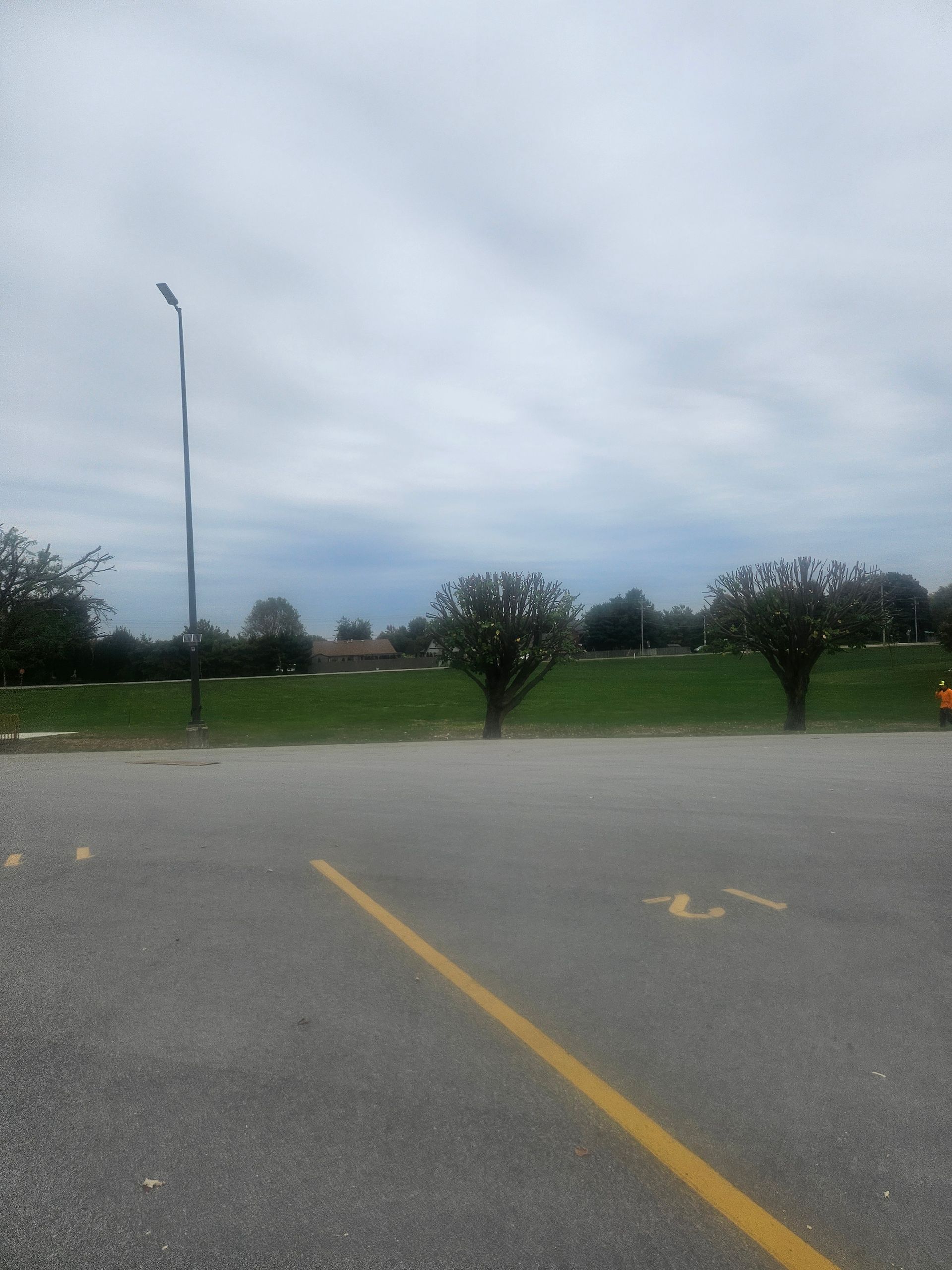 Empty parking lot beside a grassy field under cloudy sky