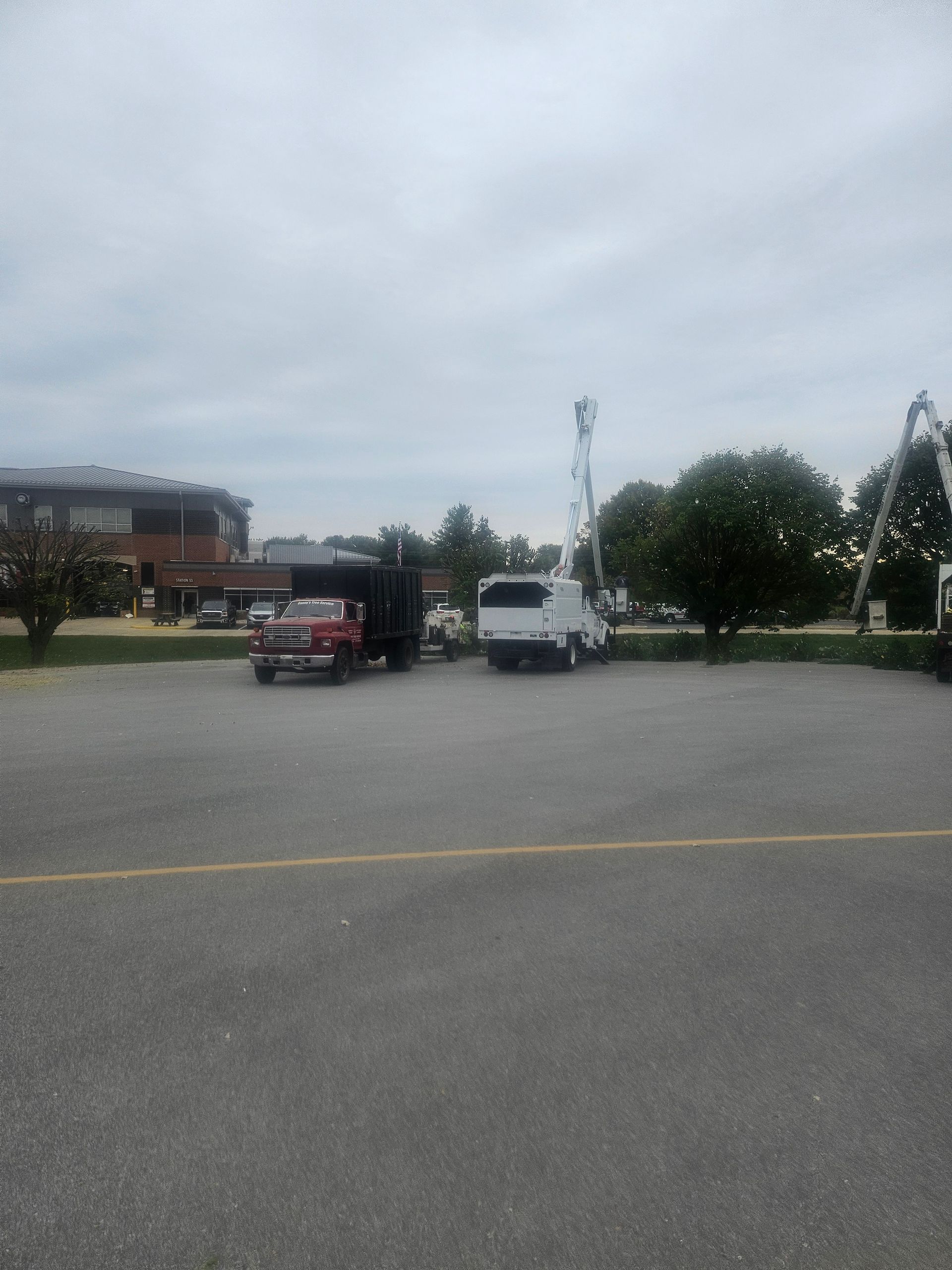 Parking lot with a red truck and white van near a building under a cloudy sky