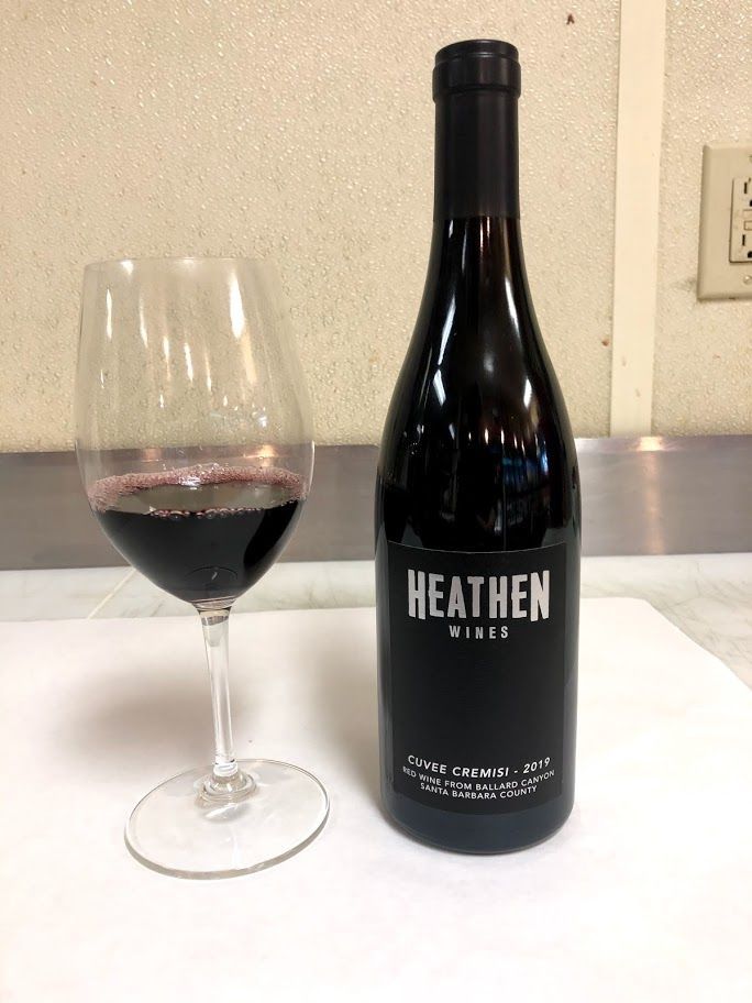 Wine glass with red wine next to a dark wine bottle labeled