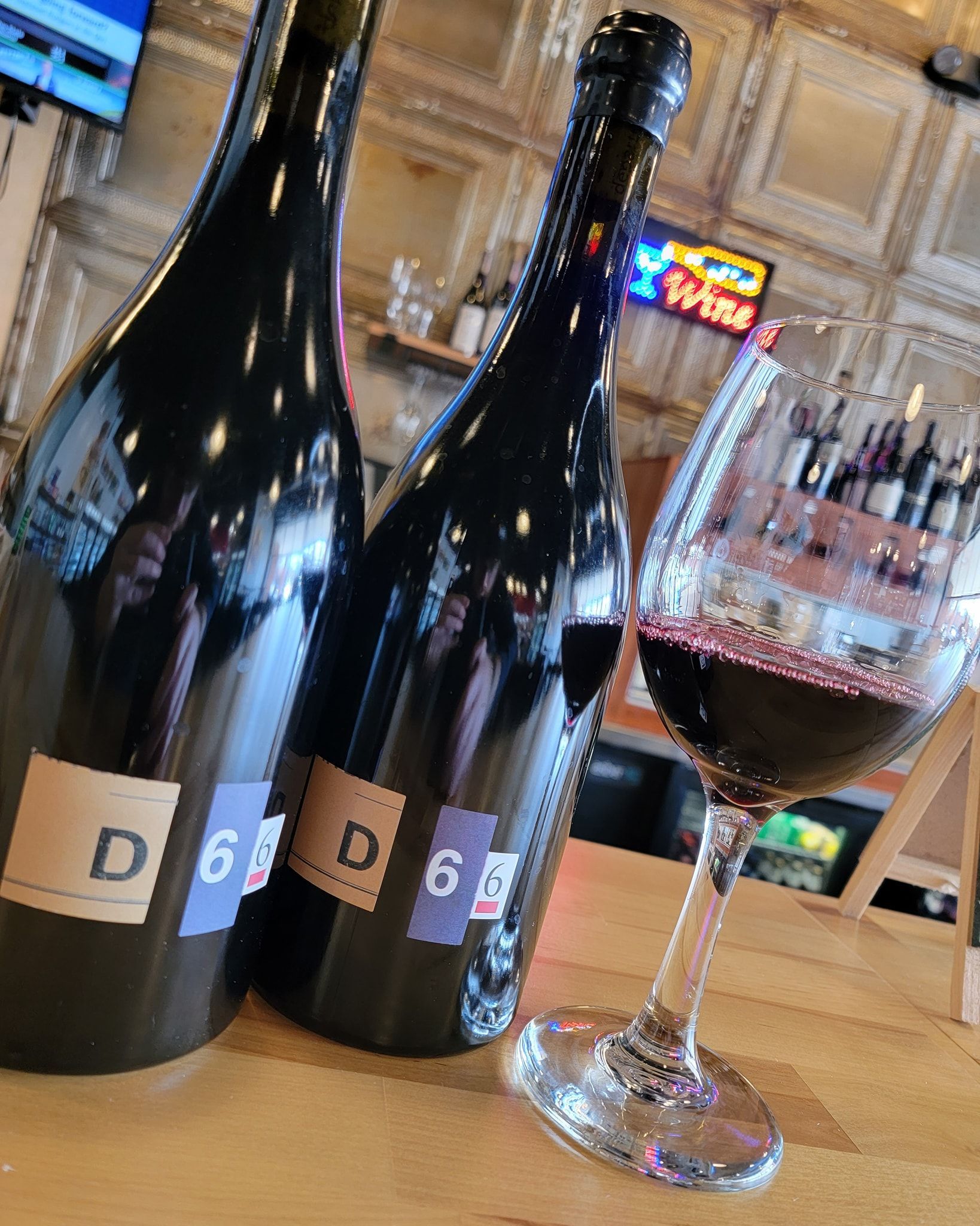 Two wine bottles and a glass of red wine on a wooden bar.