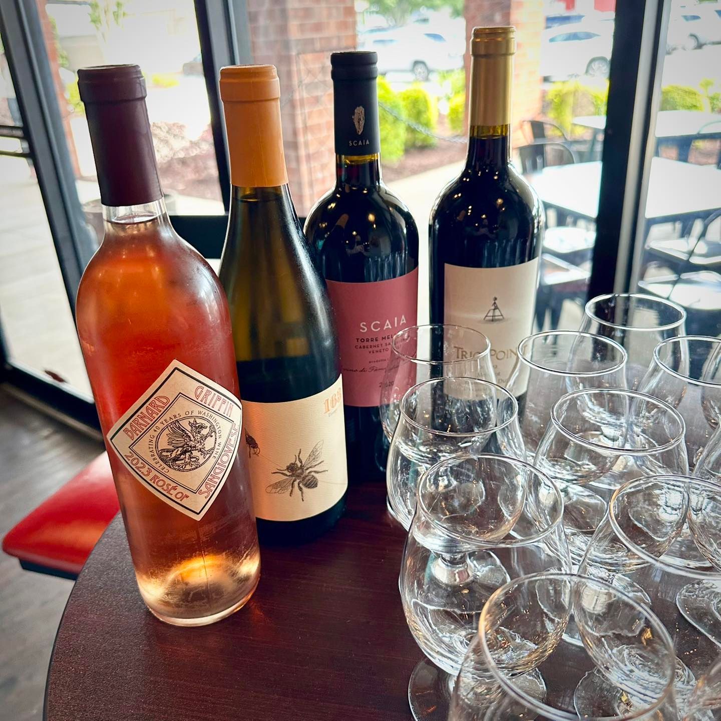 Four wine bottles with a stack of wine glasses on a table.