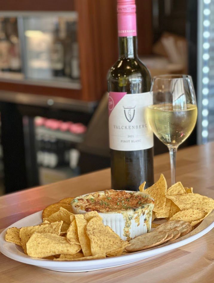 Appetizer with chips, wine bottle, and a full glass of white wine on a table.