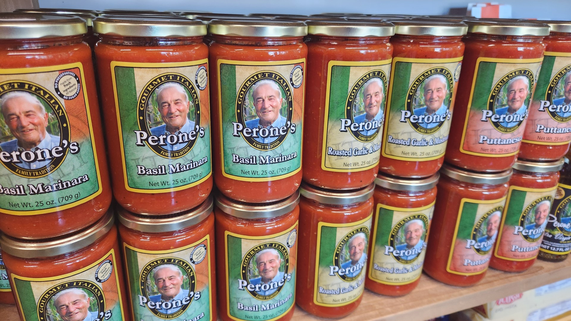 Jars of Perone's pasta sauce on a shelf. Labels have a man's portrait and different sauce flavors, mostly red.