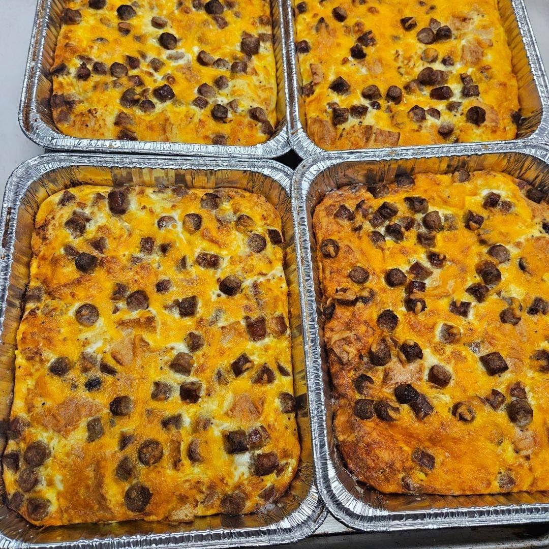 Four aluminum pans of sausage and egg casserole, golden brown with dark sausage pieces.