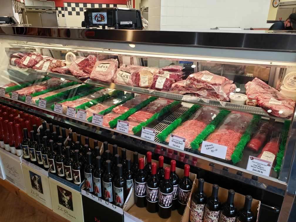 Meat display case filled with various cuts of raw meat, with bottles of wine below.