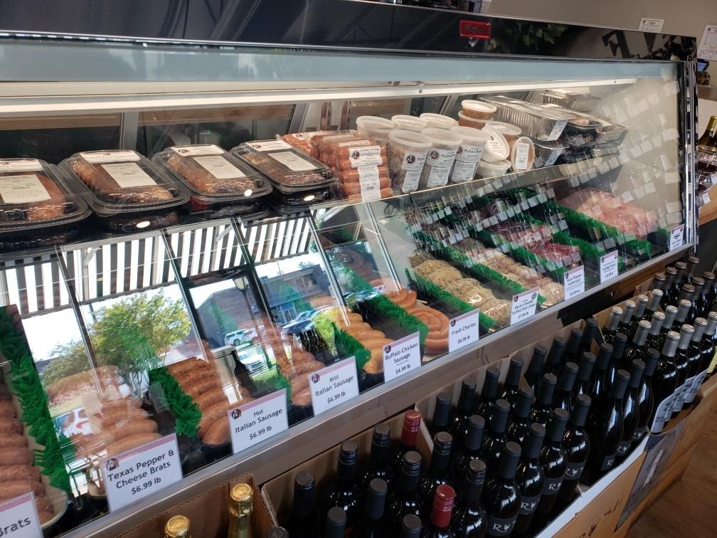 A deli display case with various meats and cheeses, and bottles of wine.