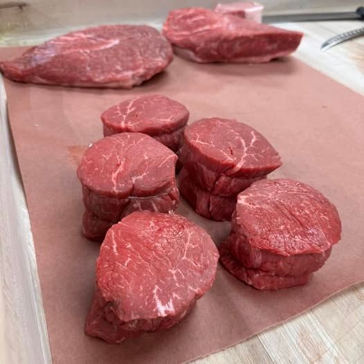 Raw cuts of beef, including filet mignon and steaks, on a butcher paper-lined surface.