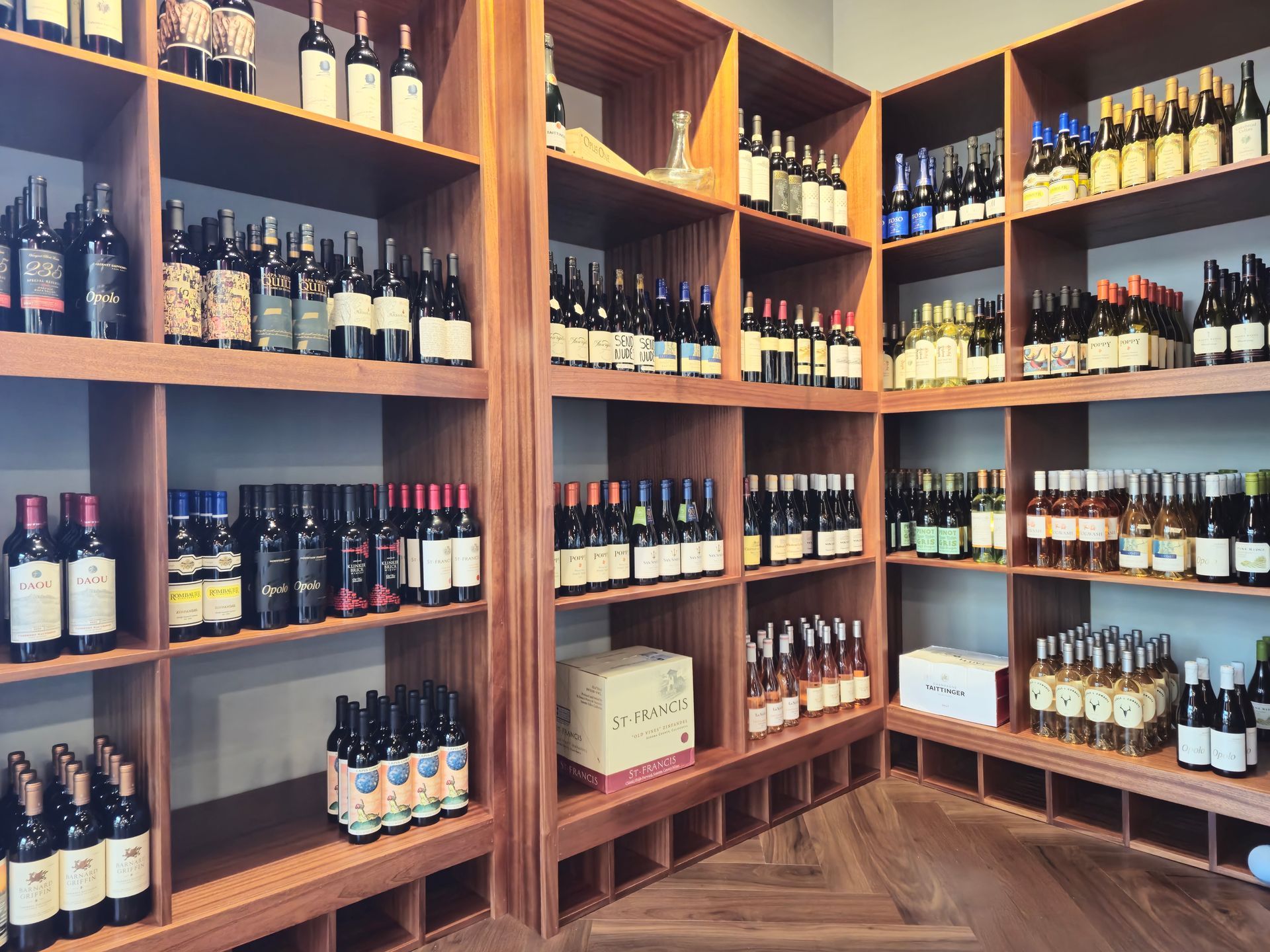 Shelves filled with wine bottles in a store; wooden shelves, various colors and labels.