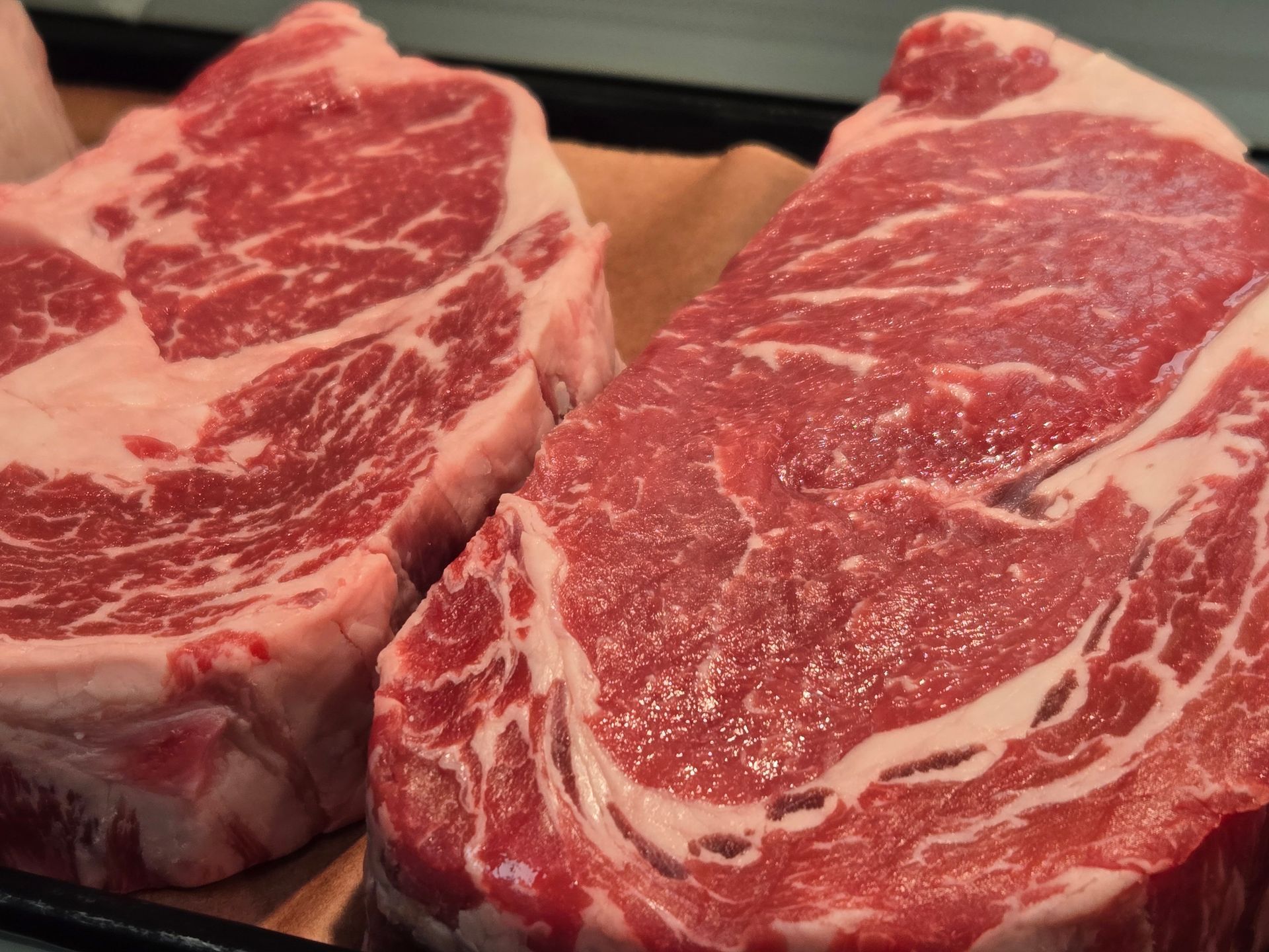 Two raw ribeye steaks, showing marbling, on a tray.