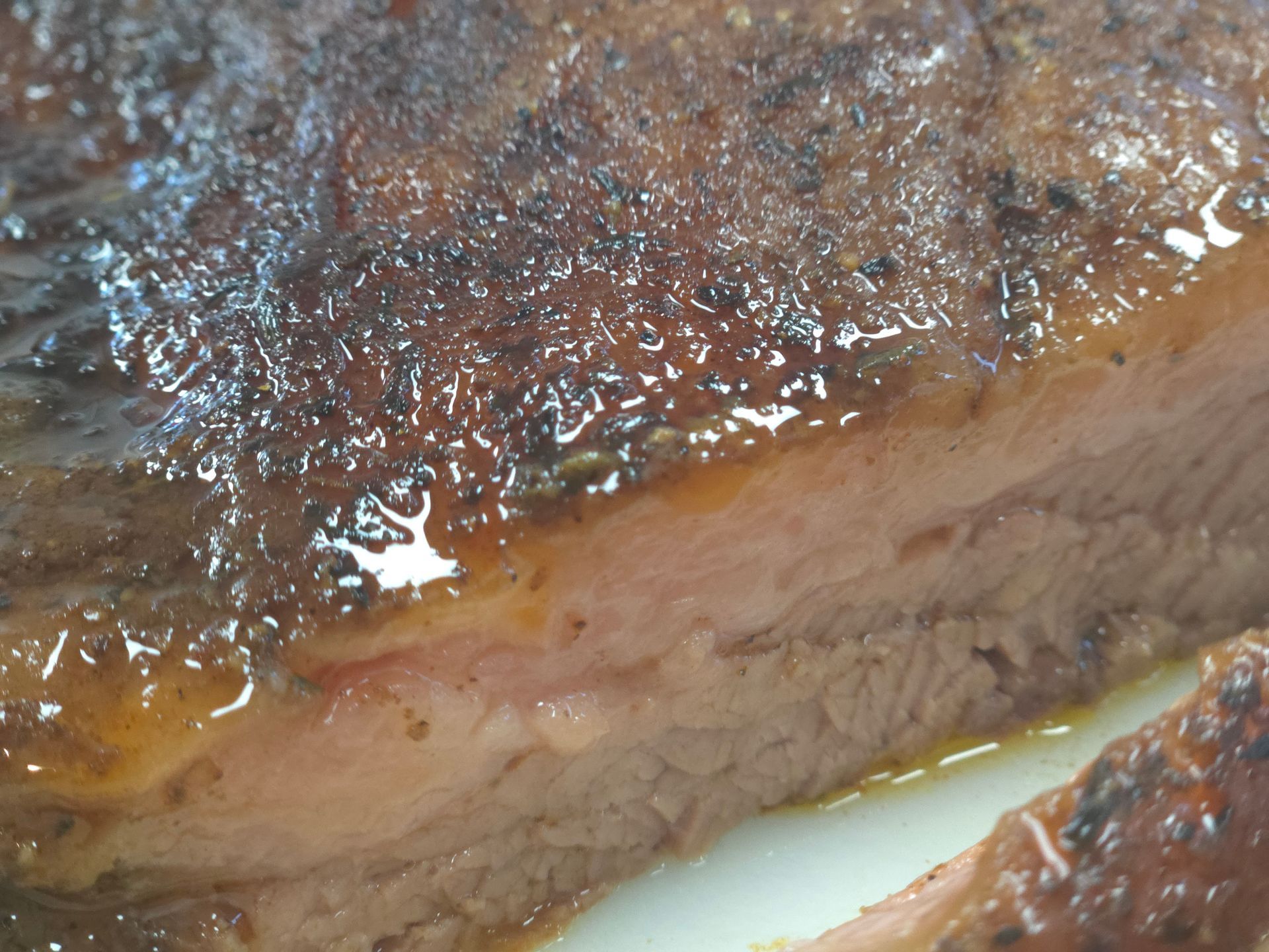 Close-up of cooked ribs, showing a moist, glazed surface and tender meat with visible fat.