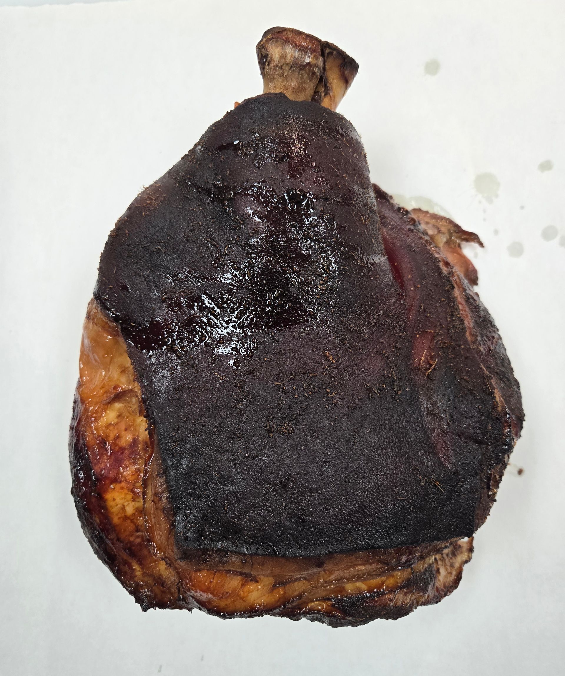 Roasted pork knuckle with dark, crispy skin on white surface.