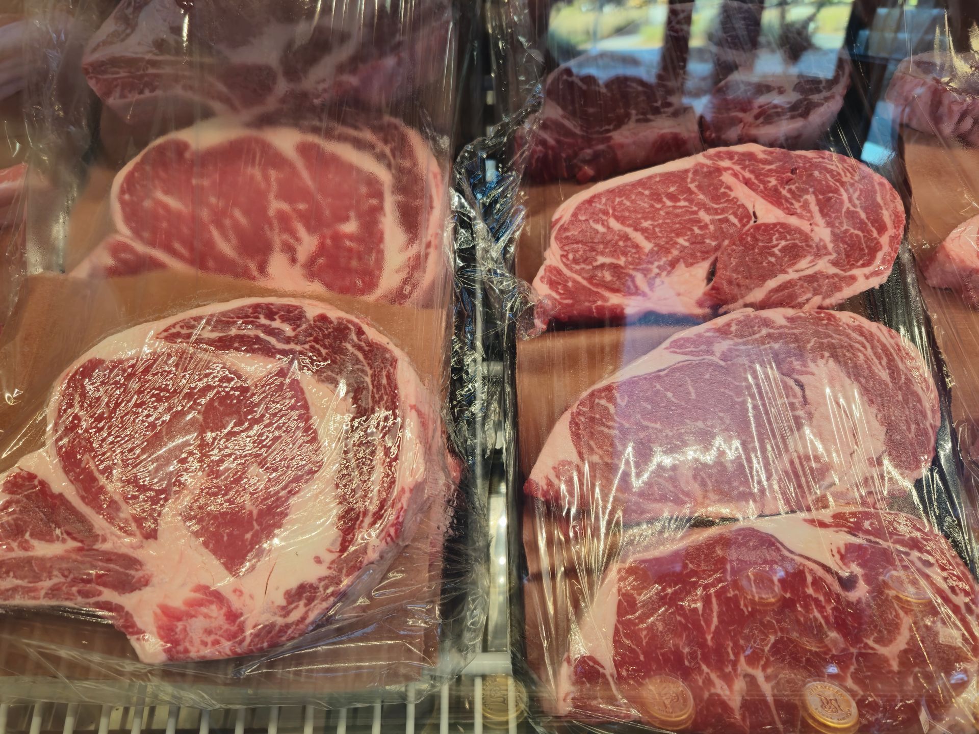 Raw ribeye steaks in a refrigerated display, wrapped in plastic.