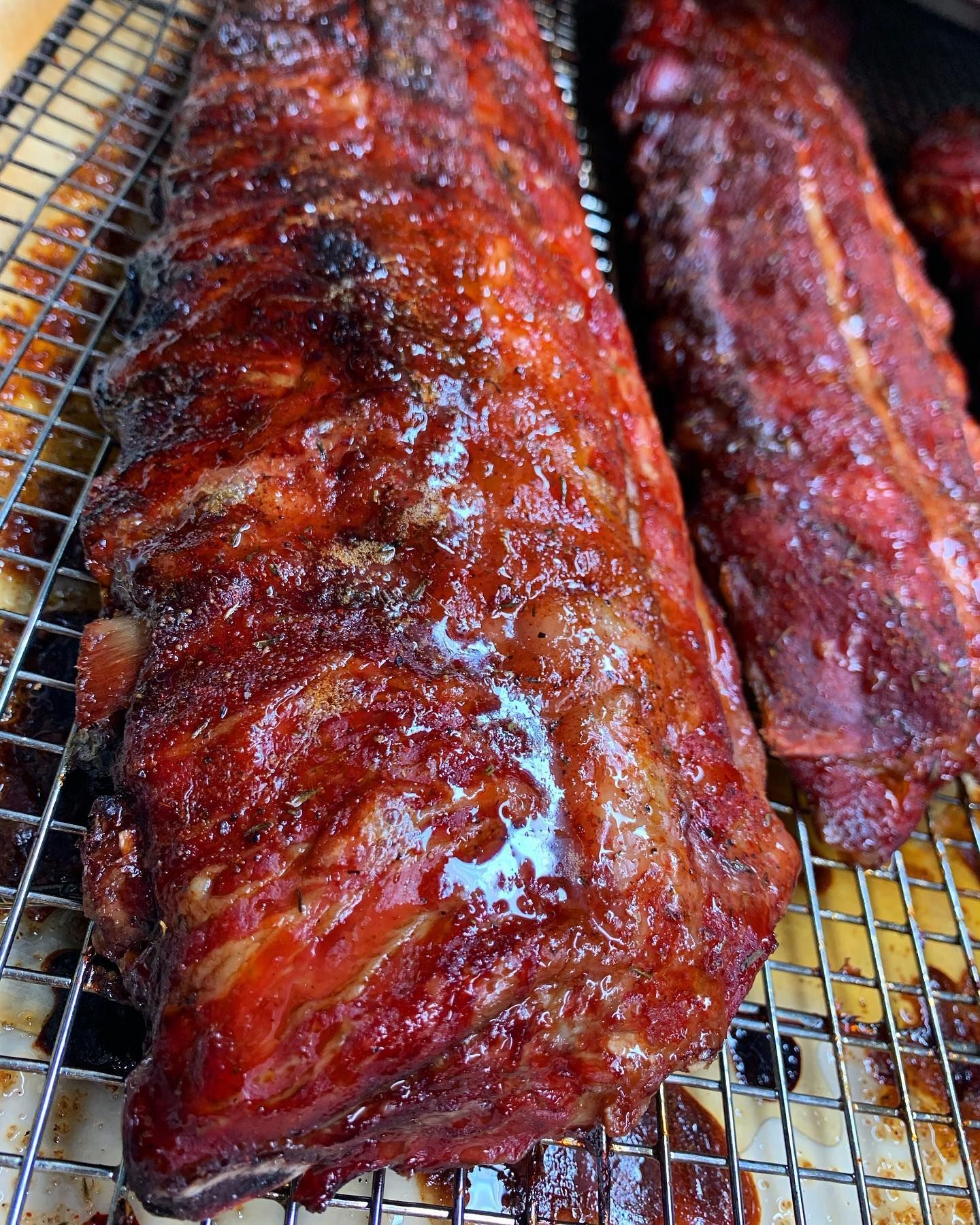 Rack of smoked ribs, glossy and red-brown, on a wire rack.