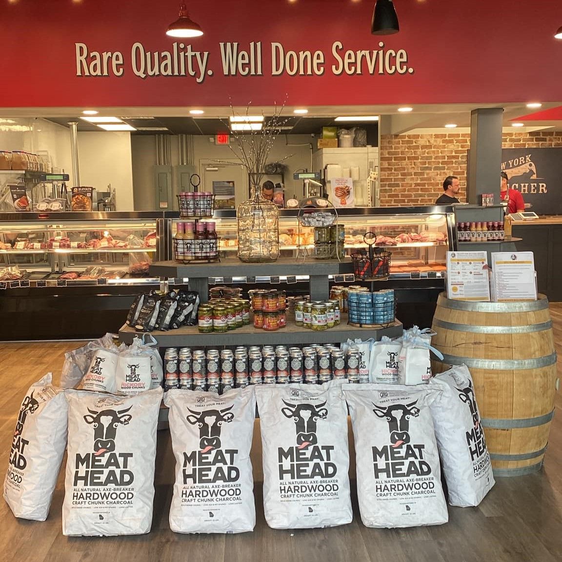 Interior of a butcher shop with meat, drinks, and bags of grilling charcoal. Overhead sign: