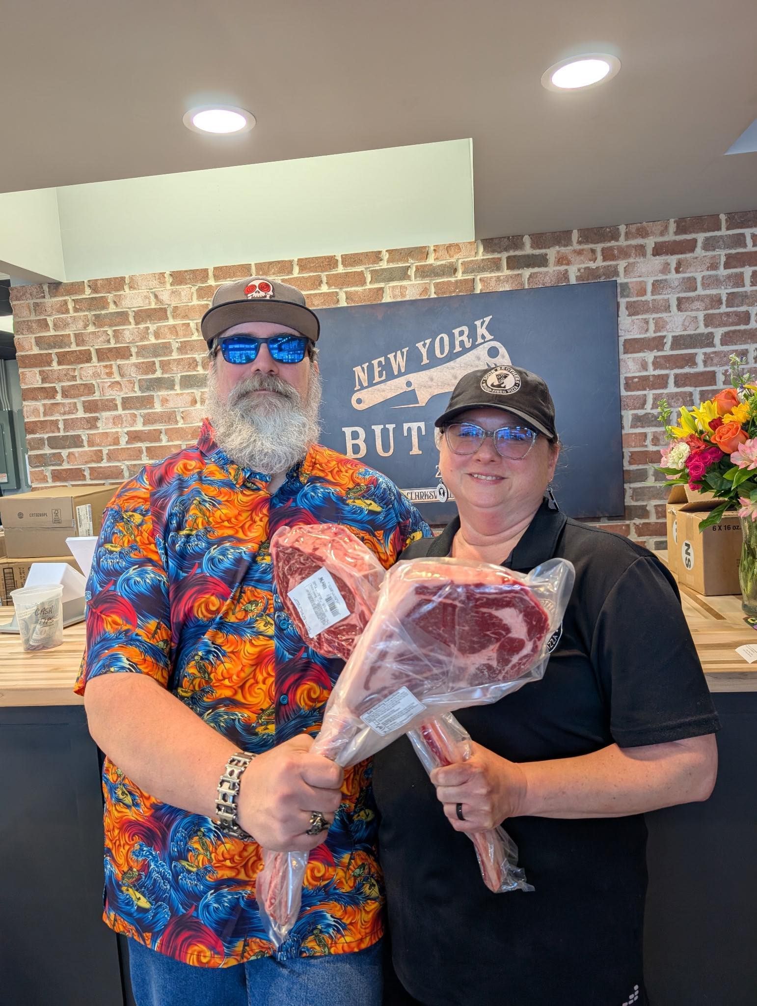 Two people in butcher shop holding large cuts of raw meat.