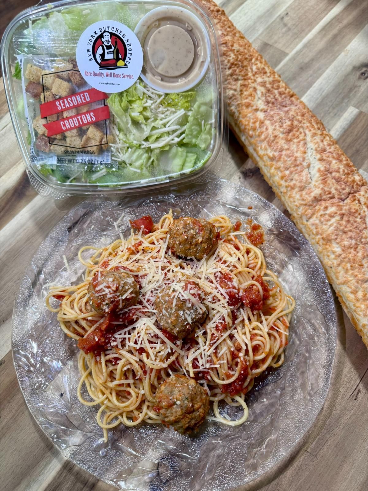 Spaghetti with meatballs, Caesar salad, and bread on a wood table.