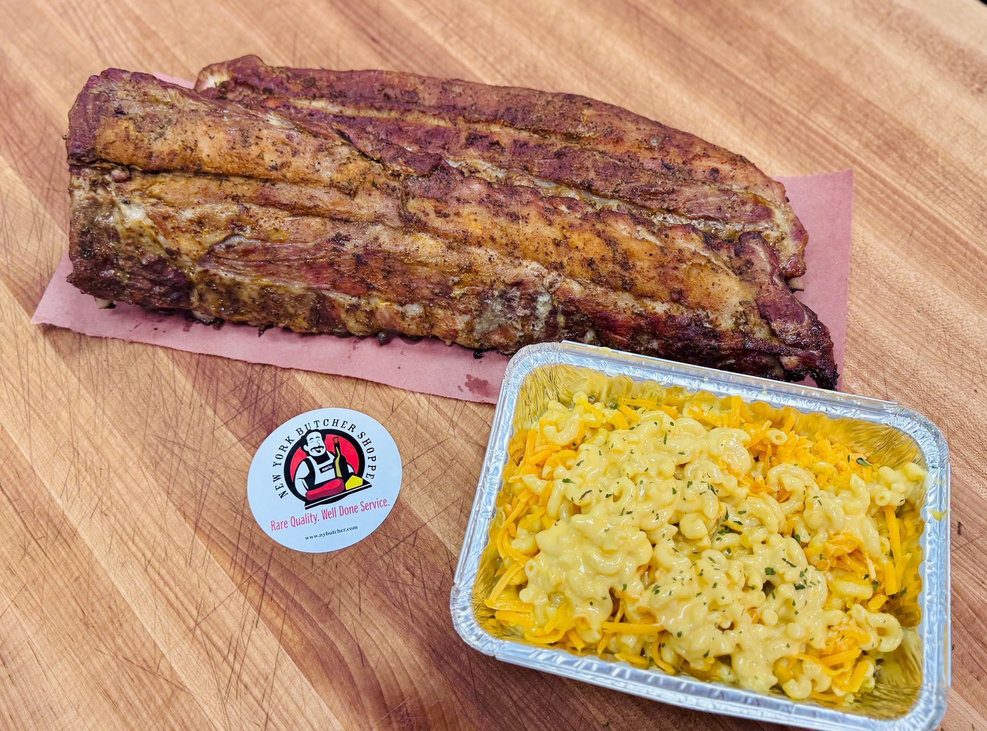 Smoked pork belly and mac and cheese in a foil tray on a wooden surface.