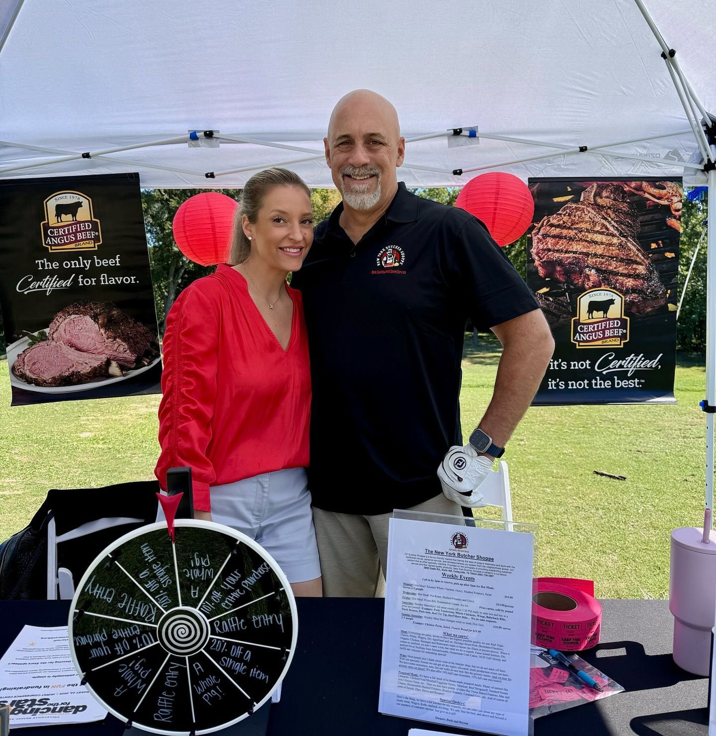 Two people pose at a booth with beef branding. The woman wears red, the man wears black. They stand in front of a tent.
