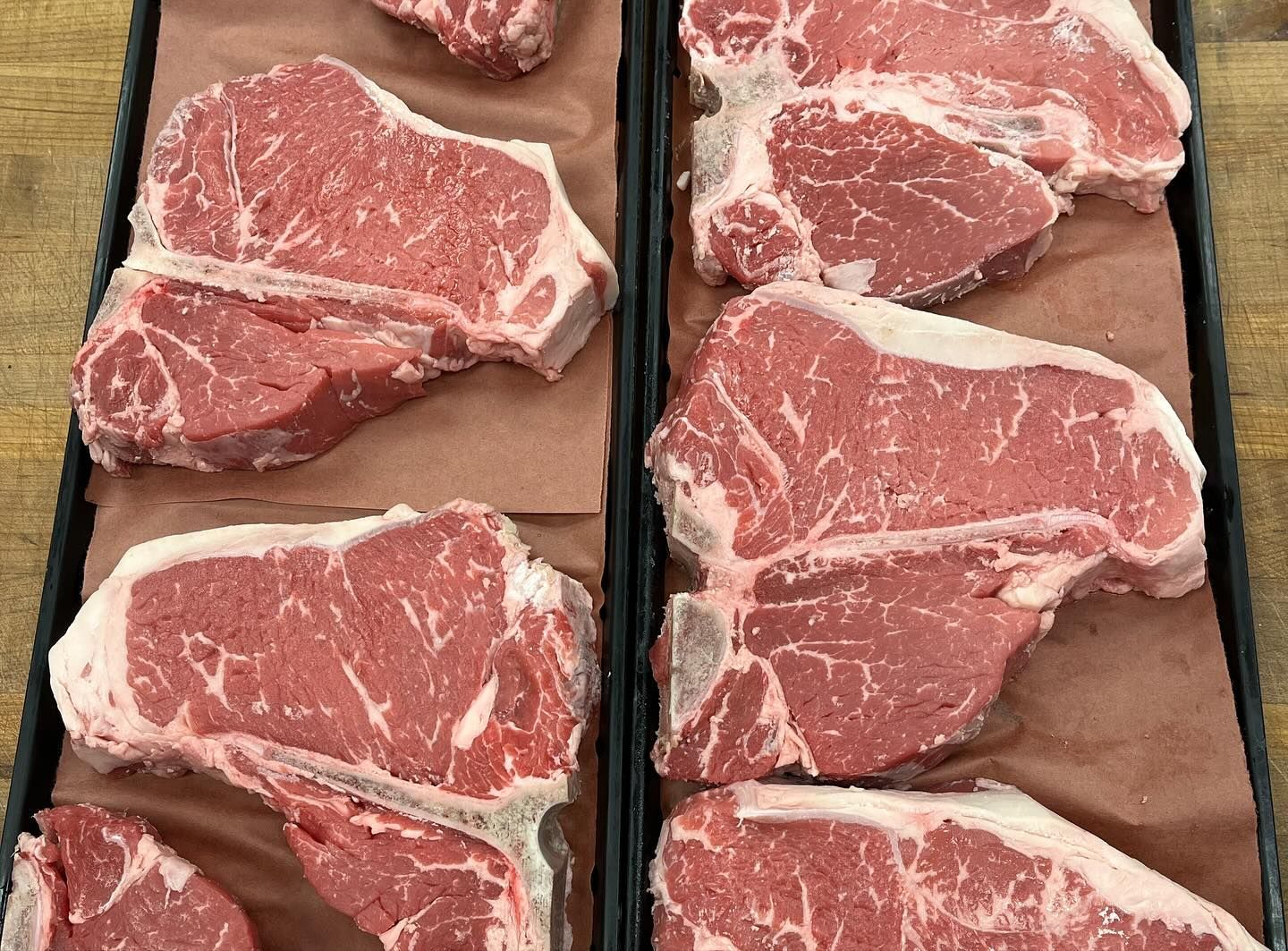 Raw T-bone steaks arranged in trays on brown paper, ready for purchase.