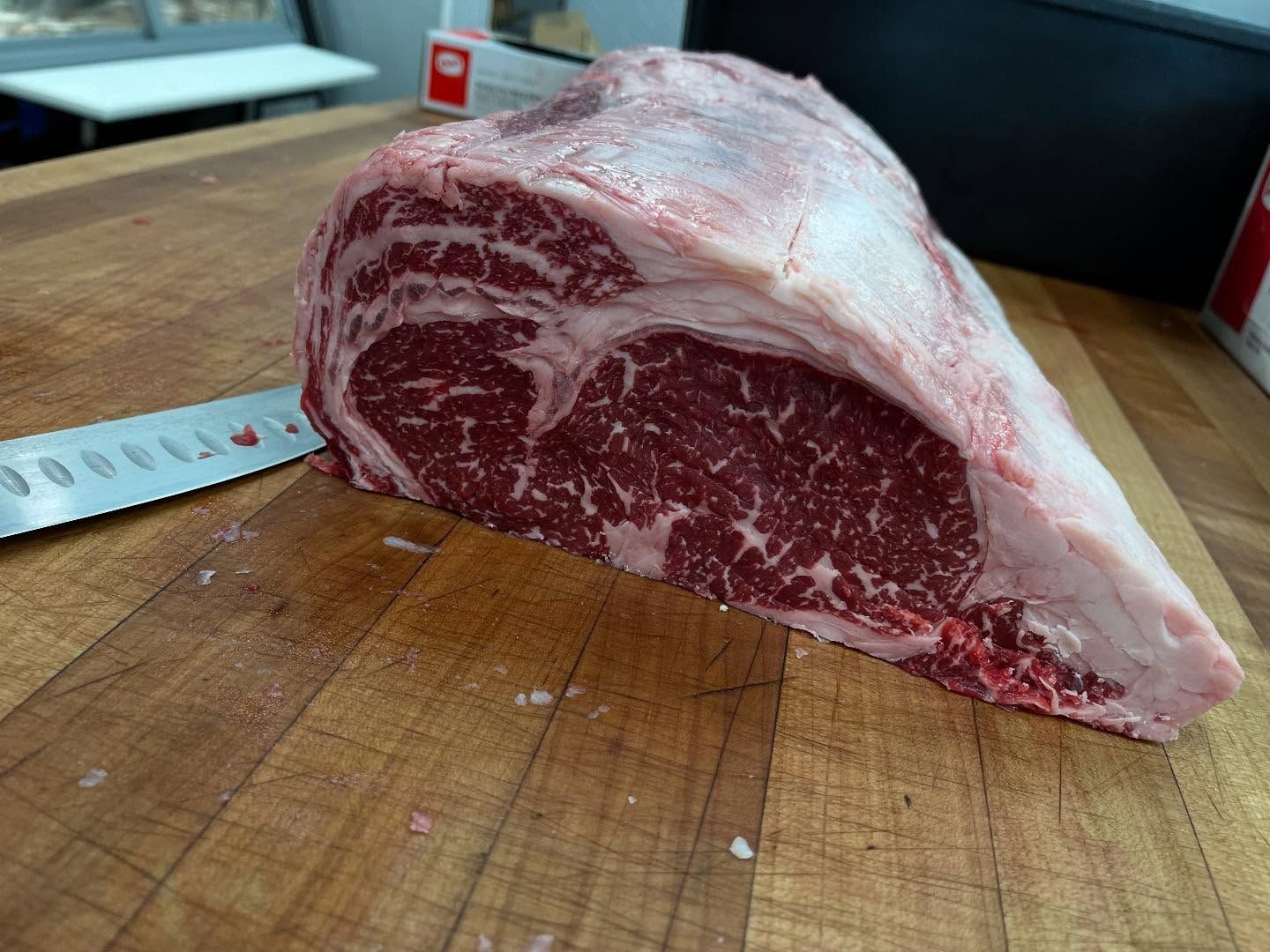 Large raw ribeye roast on a wooden butcher block, with a knife beside it.