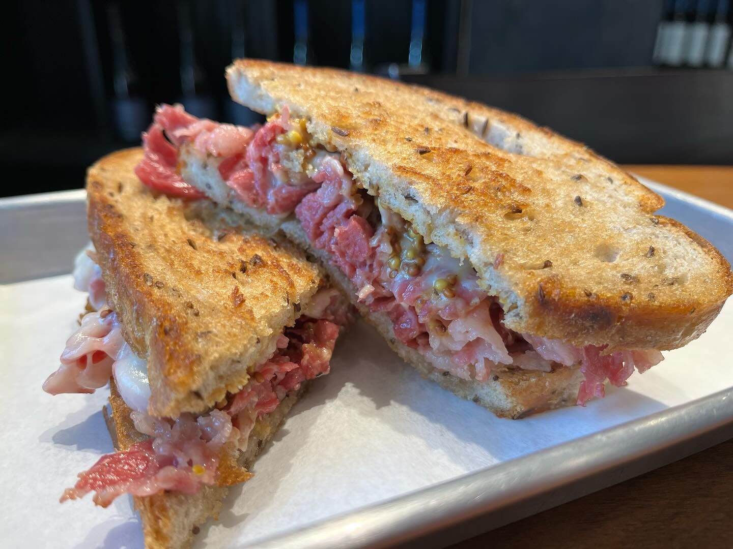 Reuben sandwich, toasted bread, corned beef, mustard, sliced on a tray.
