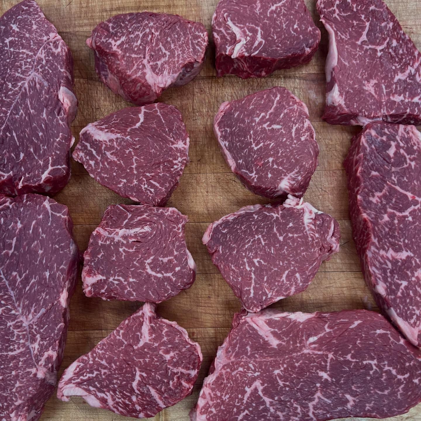 Raw, cut steaks arranged on a wooden surface, showing marbled fat and deep red color.