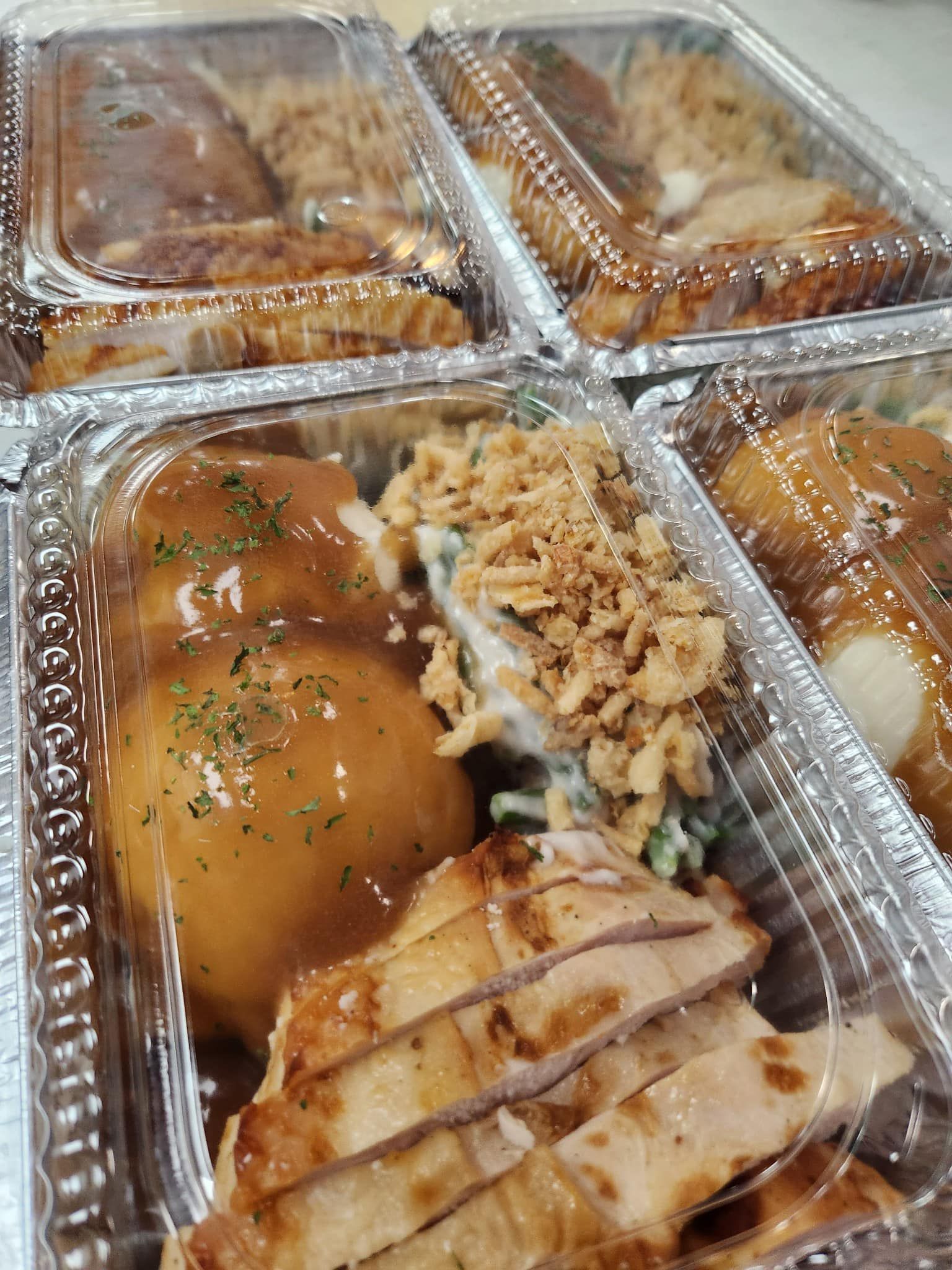 Grilled chicken with mashed potatoes, green beans, and gravy, in a clear container.