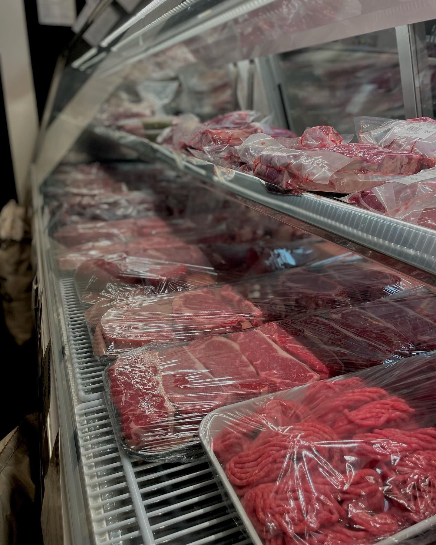 Meat display case filled with various cuts of fresh, red meat, all wrapped in plastic.