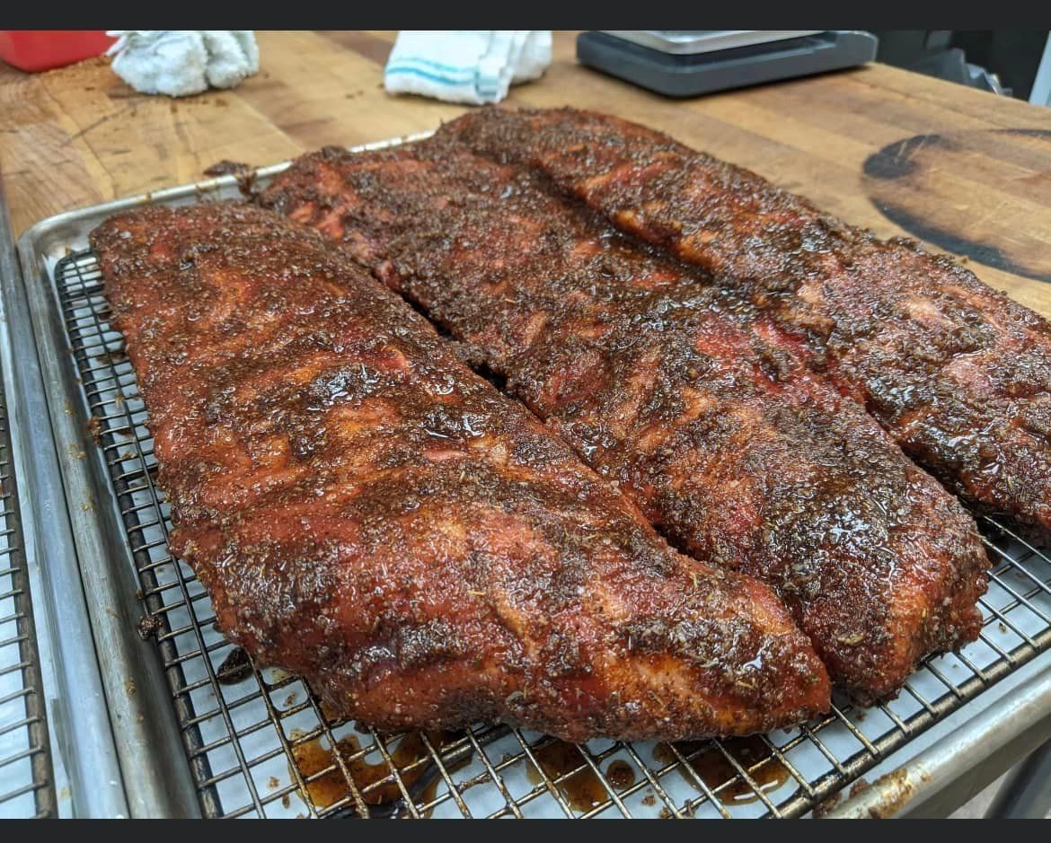 Rack of smoked ribs, seasoned with spices, on a metal rack, indoors.