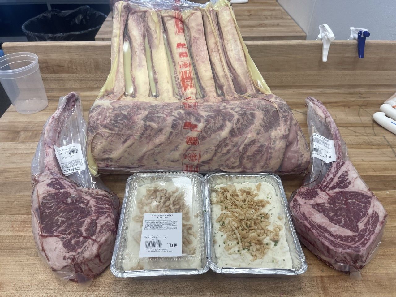 Ribeye steaks and side dishes arranged on a butcher block counter.